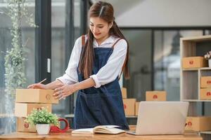 spedizione shopping in linea ,giovane inizio su piccolo attività commerciale proprietario scrittura indirizzo su cartone scatola a luogo di lavoro.piccolo attività commerciale imprenditore pmi o libero professionista asiatico donna Lavorando con scatola a ufficio foto