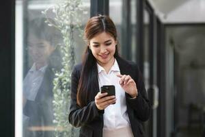 affascinante donna asiatica con un sorriso in piedi in possesso di documenti e telefono cellulare in ufficio. foto