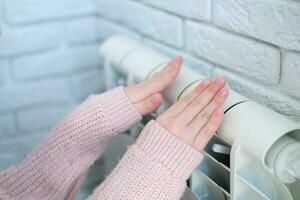 il bambino è mani caldo loro mani vicino il riscaldamento termosifone. Salvataggio gas nel il riscaldamento stagione. foto