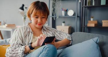 giovane signora asiatica che utilizza un messaggio di testo dello smartphone o controlla i social media sul divano nel soggiorno di casa foto