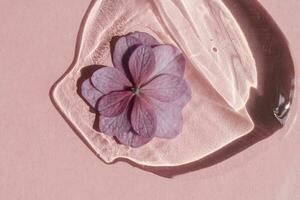 un' far cadere di trasparente cosmetico gel con fiore su un' rosa sfondo. foto