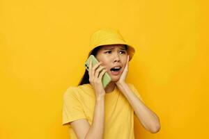 donna con asiatico aspetto nel un' giallo cappello e maglietta parlando su il Telefono giallo sfondo inalterato foto
