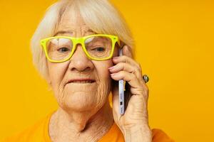 sorridente anziano donna contento stile di vita nel giallo magliette con Telefono avvicinamento emozioni foto