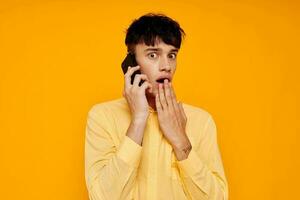 giovane tipo nel giallo camicia parlando su il Telefono isolato sfondo foto