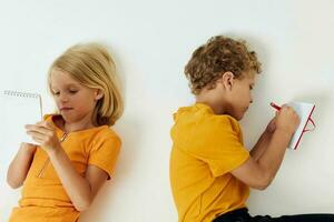 Due gioioso bambini menzogna su il pavimento con taccuini e matite isolato sfondo inalterato foto