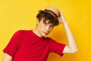 ritratto di un' giovane Riccio uomo emozioni rosso maglietta cappello studio giallo sfondo inalterato foto
