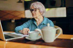 contento anziano donna Lavorando nel davanti di il computer portatile tenere sotto controllo seduta stile di vita inalterato foto