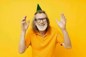 anziano dai capelli grigi uomo indossare bicchieri verde berretto su il suo testa vacanza emozioni giallo sfondo foto