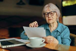 anziano donna Lavorando nel davanti di il computer portatile tenere sotto controllo seduta pensionato donna chat inalterato foto