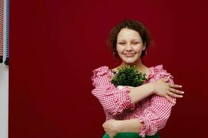 allegro donna con un' fiore nel un' pentola nel sua mani rosso sfondo inalterato foto