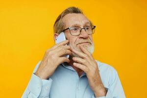 foto di pensionato vecchio uomo grigio barba con bicchieri parlando su il Telefono giallo sfondo
