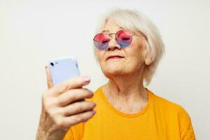 sorridente anziano donna nel un' giallo maglietta in posa comunicazione di Telefono avvicinamento emozioni foto