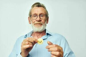 anziano dai capelli grigi uomo finanza oro monete bitcoin in posa leggero sfondo foto