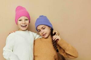 Due poco ragazze nel maglioni e cappelli abbraccio amicizia beige sfondo foto