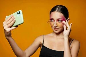 alla moda donna luminosa trucco in posa nero maglia con un' Telefono nel mano isolato sfondo inalterato foto