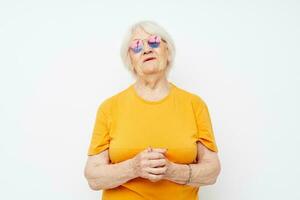 ritratto di un vecchio amichevole donna nel casuale maglietta occhiali da sole leggero sfondo foto