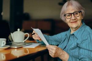 anziano donna con bicchieri si siede a un' tavolo nel davanti di un' il computer portatile libero professionista lavori inalterato foto