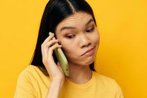 affascinante giovane asiatico donna parlando su il Telefono in posa tecnologia giallo sfondo inalterato foto