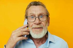 ritratto di contento anziano uomo grigio barba con bicchieri parlando su il Telefono giallo sfondo foto