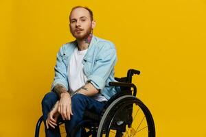 un' uomo nel un' sedia a rotelle sembra a il telecamera, con tatuaggi su il suo braccia si siede su un' giallo studio sfondo, il concetto di Salute è un' persona con disabilità foto