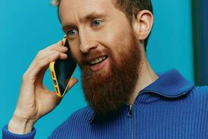 ritratto di un' uomo con un' Telefono nel il suo mani fa guardare a esso e parlando su il Telefono, su un' blu sfondo. comunicare in linea sociale media, stile di vita foto