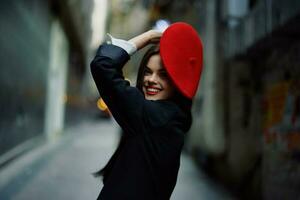 moda donna Sorridi con denti e divertimento turista nel elegante Abiti nel giacca e rosso berretto a piedi giù stretto città strada volante capelli, viaggiare, francese stile, cinematico colore, retrò Vintage ▾ stile. foto