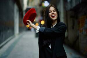 moda donna Sorridi con denti e divertimento turista nel elegante Abiti nel giacca e rosso berretto a piedi giù stretto città strada volante capelli, viaggiare, francese stile, cinematico colore, retrò Vintage ▾ stile. foto