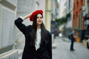 donna in piedi vicino un' parete nel il città indossare un' elegante giacca e rosso berretto con rosso labbra, viaggio e tempo libero, francese stile di vestire. foto