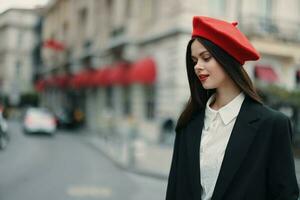 moda donna ritratto bellezza in piedi su il strada nel davanti di il città nel elegante Abiti con rosso labbra e rosso berretto, viaggiare, cinematico colore, retrò Vintage ▾ stile, urbano moda stile di vita. foto