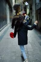 moda donna turista nel elegante Abiti nel un' giacca e rosso berretto in esecuzione giù il stretto strada di il città Sorridi e felicità viaggio, francese stile, cinematico colore. foto