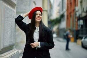 donna in piedi vicino un' parete nel il città indossare un' elegante giacca e rosso berretto con rosso labbra, viaggio e tempo libero, francese stile di vestire. foto