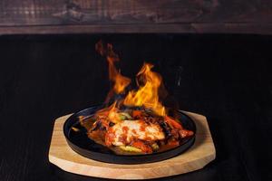 fajitos, carne in padella con fuoco su un vassoio di legno, bella porzione, sfondo scuro foto