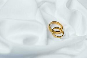 d'oro nozze anelli per Fidanzamento. matrimonio d'oro anelli con bianca, rosa nastri sfondo. anelli su il bianca e rosso rosa. il matrimonio anelli è il simbolo di tradizionale nozze di paio amanti. foto