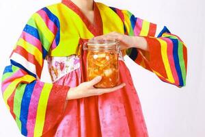 coreano donna indossare hanbok detiene un' bottiglia di kimchi con bianca cavolo, carota, ravanello, cipolla, Zenzero, mela, chili e sale è un' delizioso fermentato cibo foto