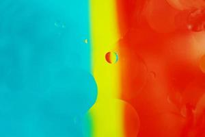 una bella e vibrante macro di bolle d'olio sull'acqua con una trama a strisce gialle, blu e rosse come motivo di sfondo con filtro vintage foto
