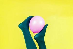 gambe verdi di una donna che tiene un palloncino rosa contro un muro giallo foto