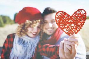 bel primo piano di un bel cuore rosso tenuto da una giovane coppia romantica innamorata in un bel bokeh come sfondo all'aperto. ricorda l'amore o l'assistenza sanitaria foto