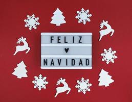 scatola leggera con frase feliz navidad, buon natale spagnolo su sfondo rosso con giocattoli in legno. foto