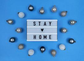 scatola luminosa con citazione di soggiorno a casa su sfondo blu con palle di Natale. foto
