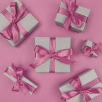 scatole regalo avvolte in carta artigianale con morbidi nastri e fiocchi rosa. festivo piatto monocromatico. foto