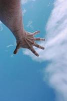 mano in alto raggiungendo il cielo azzurro foto