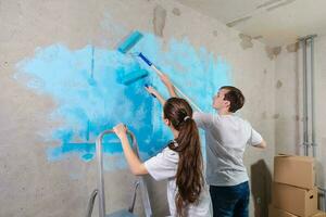 coppia nel nuovo casa durante riparazione lavori pittura parete insieme. contento famiglia Tenere dipingere rullo pittura parete con blu colore dipingere nel nuovo Casa. casa rinnovamento Fai da te rinnovare casa concetto. foto