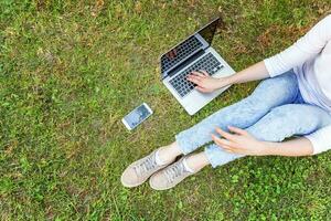 gambe di donna sul prato di erba verde nel parco cittadino, mani che lavorano su un computer portatile. concetto di business freelance foto