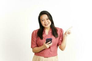 Tenere smartphone e puntamento lato utilizzando indice di bellissimo asiatico donna isolato su bianca foto