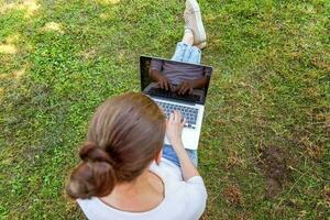 giovane donna seduta sul prato di erba verde nel parco cittadino che lavora su un computer portatile. concetto di business freelance foto