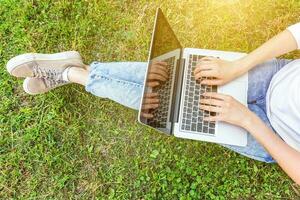 gambe di donna sul prato di erba verde nel parco cittadino, mani che lavorano su un computer portatile. concetto di business freelance foto