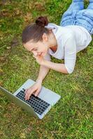 giovane donna dire bugie su verde erba prato nel città parco Lavorando su il computer portatile pc computer. libero professionista attività commerciale concetto foto