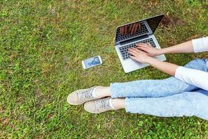 giovane donna seduta sul prato di erba verde nel parco cittadino che lavora su un computer portatile. concetto di business freelance foto