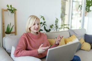 sorridente giovane donna utilizzando il computer portatile a casa, guardare a schermo, chattare, indossare senza fili cuffia avendo video conferenza . attività commerciale allenatore tutoraggio di webcam, in linea addestramento, e-coaching concetto foto