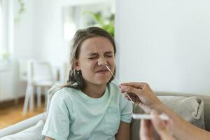 madre è assunzione rapido covid-19 test a casa per sua malato figlia a casa. mamma analisi giovane ragazza per coronavirus infezione assunzione rapido covid-19 test foto